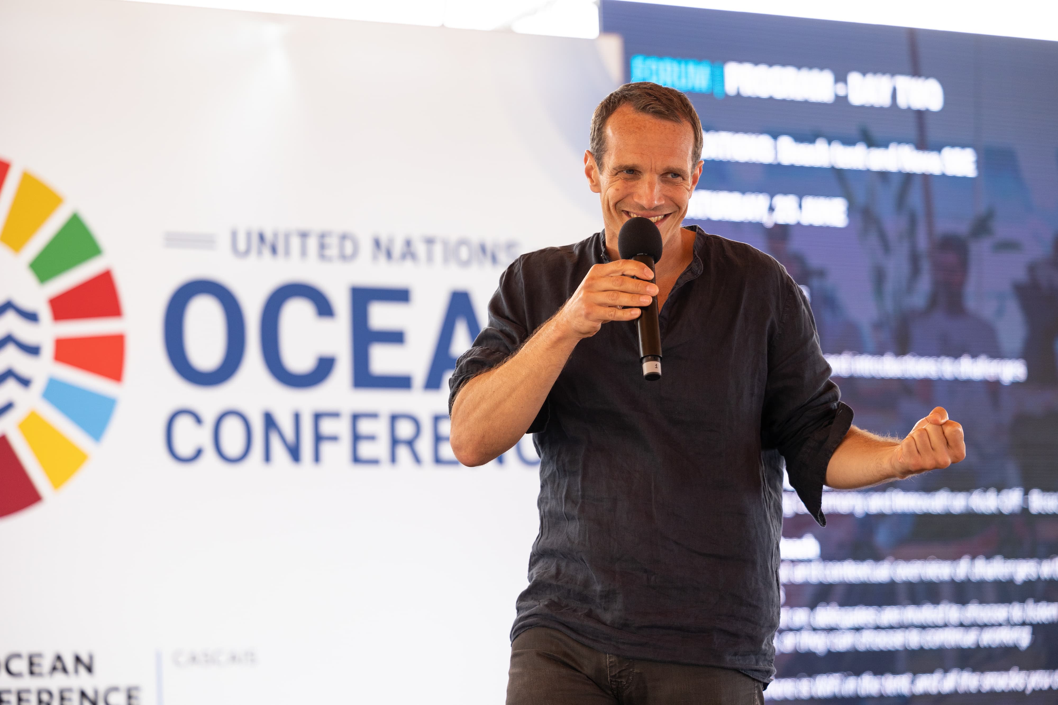 Man addressing a group on stage in front of display stand